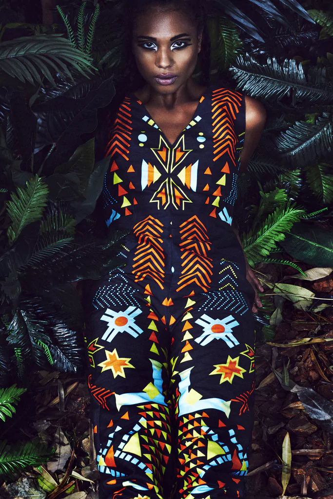 Model wearing black jumpsuit with blue and orange geometric tribal print, green studio background