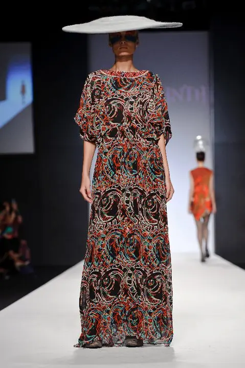 Model wearing a layered kimono-sleeve kaftan with 3D Printed Clothes of motor and turbine print in reds, blues, and blacks, featuring crinkled chiffon overlay, heavy Swarovski crystal embroidery, and a spaceship-shaped hat by Nazgul Nejmi.