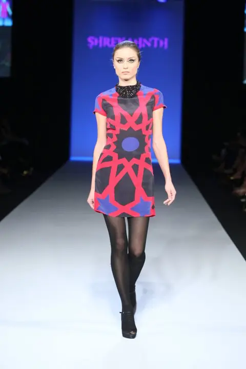Model opening the show in a short black and pink dress with bold geometric Islamic art, short sleeves, high neck, and pearl embroidery.