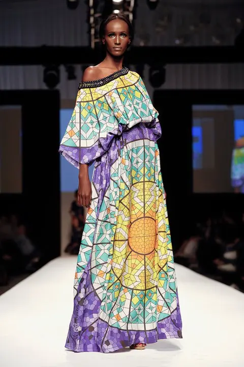 SHREKAHNTH — HOME 2026 12 Exaggerated boat neck off-shoulder kaftan in taffeta silk with stained glass print in blues, yellows, and oranges, gathered at the waist like a peplum with pearl embroidery.
