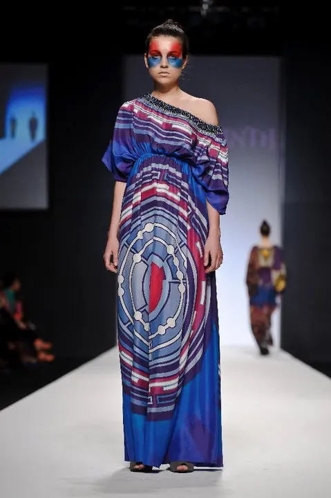 SHREKAHNTH — HOME 2026 14 Model wearing a full-length kaftan with exaggerated boat neckline embroidered with Swarovski pearls, featuring a Tron-inspired print in dark and light blues.