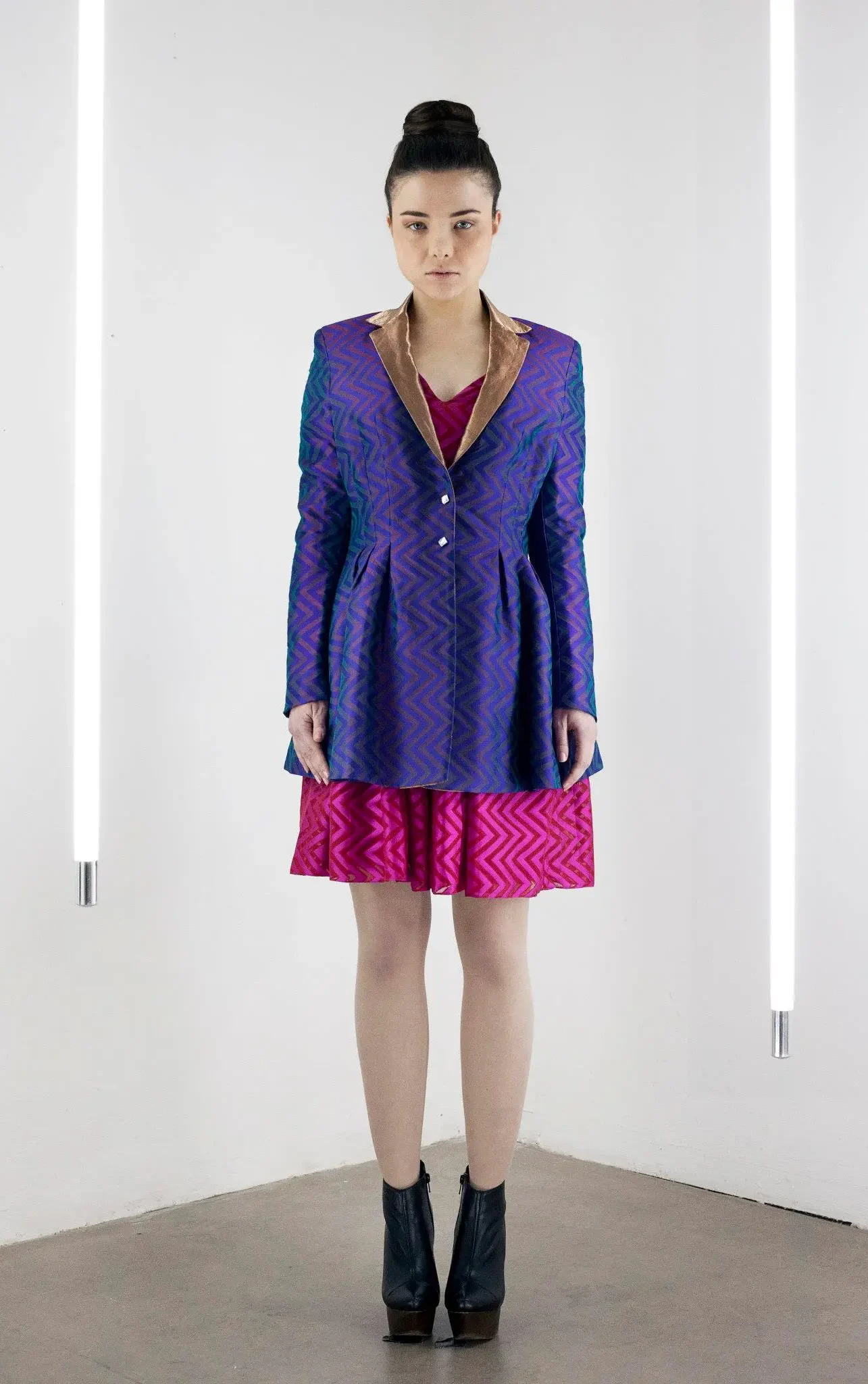 Model wearing a handwoven purple and blue pleated coat jacket with a zari collar over a pink silk dress, featuring zigzag woven patterns, shot in Berlin.