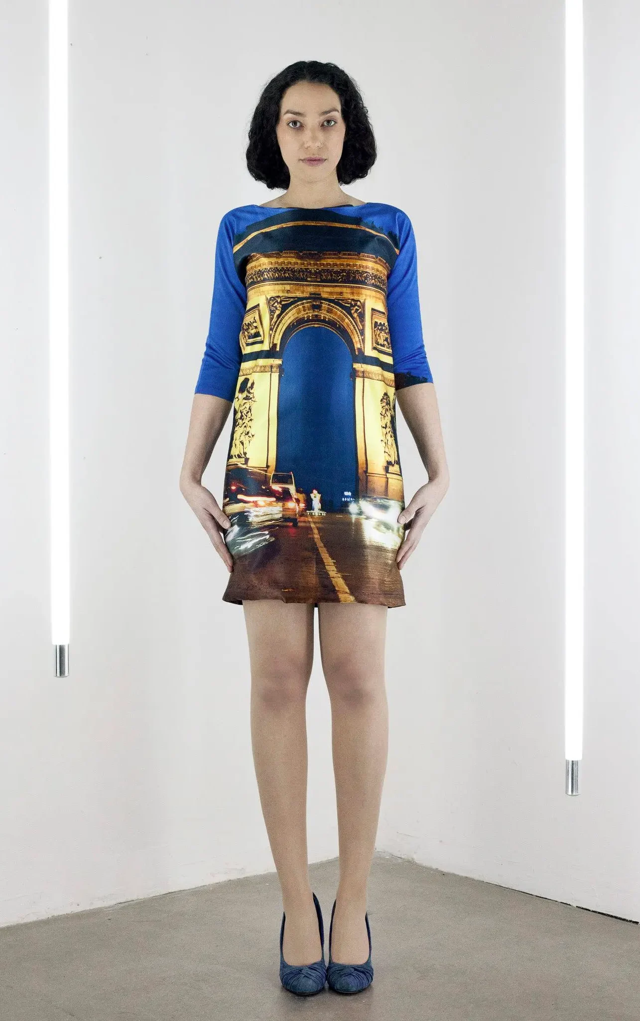 Model wearing a silk dress with a photo-realistic print of the Arc de Triomphe in Paris, set against a blue evening sky with city traffic.